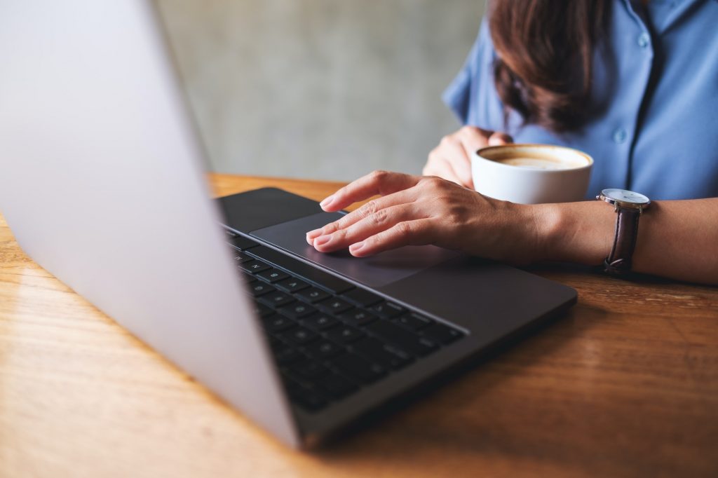 Closeup image of a woman drinking coffee while working on laptop computer